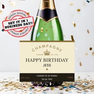 May include: A champagne bottle label with a gold and white design. The label says "Champagne" with a crown and "Fonde en 1743". It also says "Happy Birthday Jess" with a star. The label also says "Cheers to 30 years! 03.26.1992" and "12% Vol 750ml".