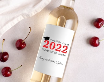 Op de afbeelding: Een fles witte wijn met een etiket met een afstudeerthema. Het etiket is wit met zwarte tekst die zegt "Cheers to the class of 2022 University of Guelph Congratulations Sophia". Het nummer 2022 is rood. Boven de tekst staat een zwart afstudeerhoedpictogram.