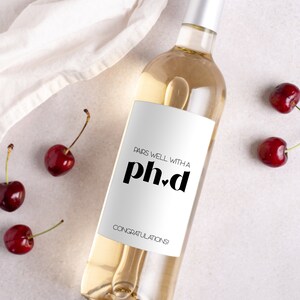 May include: A white wine bottle with a white label that says "Pairs well with a ph.d Congratulations!" The bottle is surrounded by red cherries.