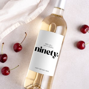 May include: A white wine bottle with a white label that says "Pairs well with turning ninety. Happy Birthday Nini".
