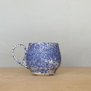 May include: A set of three ceramic mugs with a speckled, matte finish in cream, light brown, and dark brown. Each mug has a simple, minimalist design and a rounded handle.