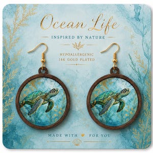 May include: Round wooden earrings with a sea turtle design. The earrings have gold-colored hooks and are set against a blue and gold background. The text "Ocean Life" and "Inspired by Nature" are visible.