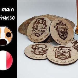 Peut inclure: Ensemble de cinq sous-verres en bois représentant les armoiries des maisons de Poudlard : Gryffondor, Poufsouffle, Serdaigle, Serpentard et un blason générique de Poudlard. Chaque sous-verre porte une devise de maison différente imprimée sous l'armoirie.
