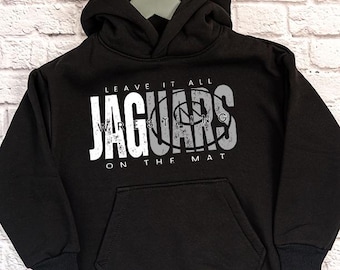 Puede incluir: Sudadera con capucha negra con un estampado gráfico blanco que dice "LEAVE IT ALL JAGUARS WRESTLING ON THE MAT".