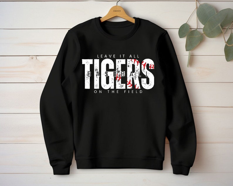 May include: Black sweatshirt with white text that reads "Leave it all Tigers Baseball on the field". The word "Tigers" is in a large font and has a red baseball graphic inside the letters.