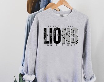 Puede incluir: Sudadera gris con texto negro que dice "Leave it all on the mat" y "Lions Wrestling".