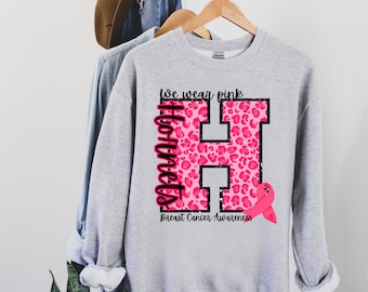 Puede incluir: Una sudadera gris con una letra H de estampado de leopardo rosa y el texto "We wear pink Hornets Breast Cancer Awareness".