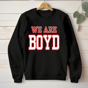 Pode incluir: Camisola de moletom preta com texto branco que diz "We Are Boyd" em letras vermelhas com contorno.