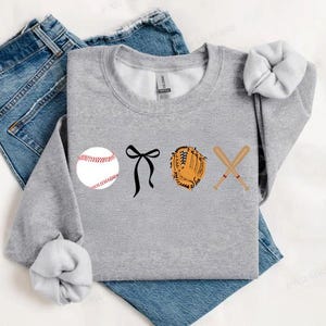 May include: Gray sweatshirt with a baseball, a black bow, a baseball glove, and two crossed baseball bats printed on the front.