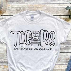 May include: White t-shirt with black text that says "TIGERS" with a school bus and pencil graphic. The text below says "LAST DAY OF SCHOOL 2023-2024".