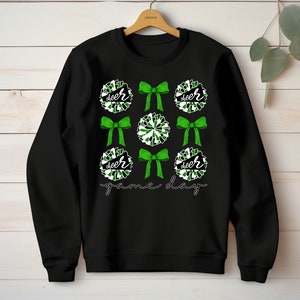 May include: Black sweatshirt with a green and white cheerleading pom-pom design. The text "cheer" and "game day" is printed on the sweatshirt.