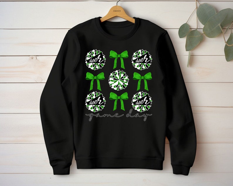 May include: Black sweatshirt with a green and white cheerleading pom-pom design. The text "cheer" and "game day" is printed on the sweatshirt.