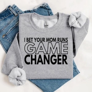 Könnte beinhalten: Grauer Pullover mit schwarzem Text, der "I bet your mom runs GAME CHANGER" lautet.