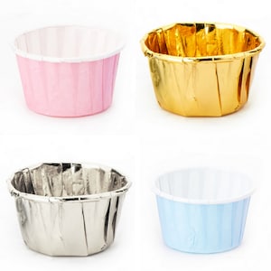 May include: Four cupcake liners in different colors: pink, gold, silver, and light blue. The liners are made of paper and have a fluted design.