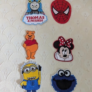 May include: A collection of six embroidered character patches featuring Thomas the Tank Engine with the text Thomas & Friends, a red Spider-Man mask, Winnie the Pooh, Minnie Mouse with a red bow, a yellow Minion, and a blue Cookie Monster character.