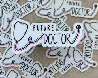 May include: A pile of white stickers featuring the words "FUTURE DOCTOR" and a stethoscope graphic. The stethoscope is outlined in black, with red and blue detailing. The stickers are spread across a light-toned background.