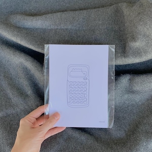 May include: A black and white line drawing of a vintage calculator on white paper, encased in a clear plastic sleeve. The image is held against a gray fabric background.