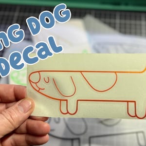 Könnte beinhalten: Ein rechteckiger Aufkleber mit einem Cartoon-Hund-Design. Der Hund ist orange umrandet mit einem hellorangen Farbverlauf. Der Aufkleber hat die Worte "LONG DOG DECAL" in blauen Buchstaben.