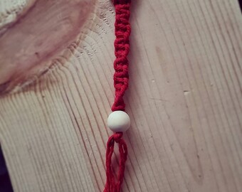 May include: A red macrame keychain with a wooden bead and a wooden ring at the top.