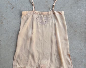 May include: A peach-colored sleeveless camisole top featuring thin shoulder straps, a straight neckline, and a scalloped hemline. The upper chest area is decorated with delicate tonal embroidery and cutwork detailing in a floral pattern.