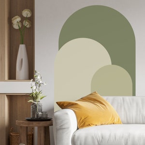 May include: A white couch with a yellow throw pillow in front of a wall with a green, beige, and cream abstract arch design.