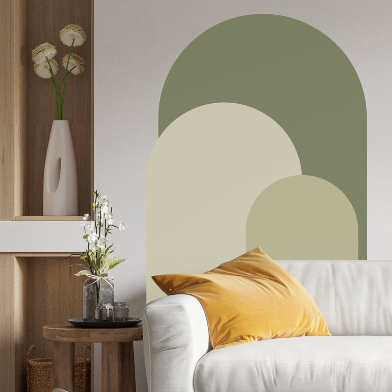 May include: A white couch with a yellow throw pillow in front of a wall with a green, beige, and cream abstract arch design.