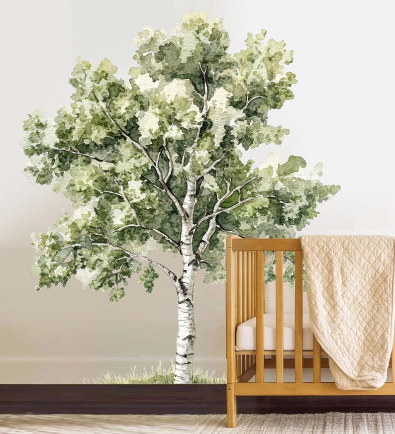 May include: Watercolor mural of a birch tree with green leaves and a white trunk. The tree is painted on a light beige wall. A wooden crib with a beige blanket is in the foreground.