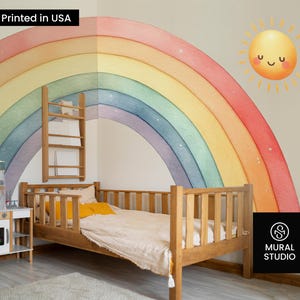 May include: A children's bedroom featuring a wooden bed, a toy kitchen, and a large rainbow wall mural. The mural depicts a watercolour rainbow and a smiling sun. The text "Printed in USA" is visible.