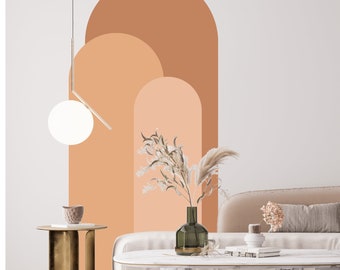 Puede incluir: Un diseño de interior de sala de estar con una pared blanca que presenta una gran calcomanía de pared abstracta de tres arcos en tonos naranja y melocotón. Una lámpara colgante de globo blanco cuelga del techo. Un sofá blanco con un cojín beige se encuentra frente a la pared. Una mesa de café con una tapa de mármol se encuentra frente al sofá. Una mesa auxiliar de metal dorado con una tapa redonda se encuentra junto al sofá. Un jarrón con flores secas se encuentra sobre la mesa de café.