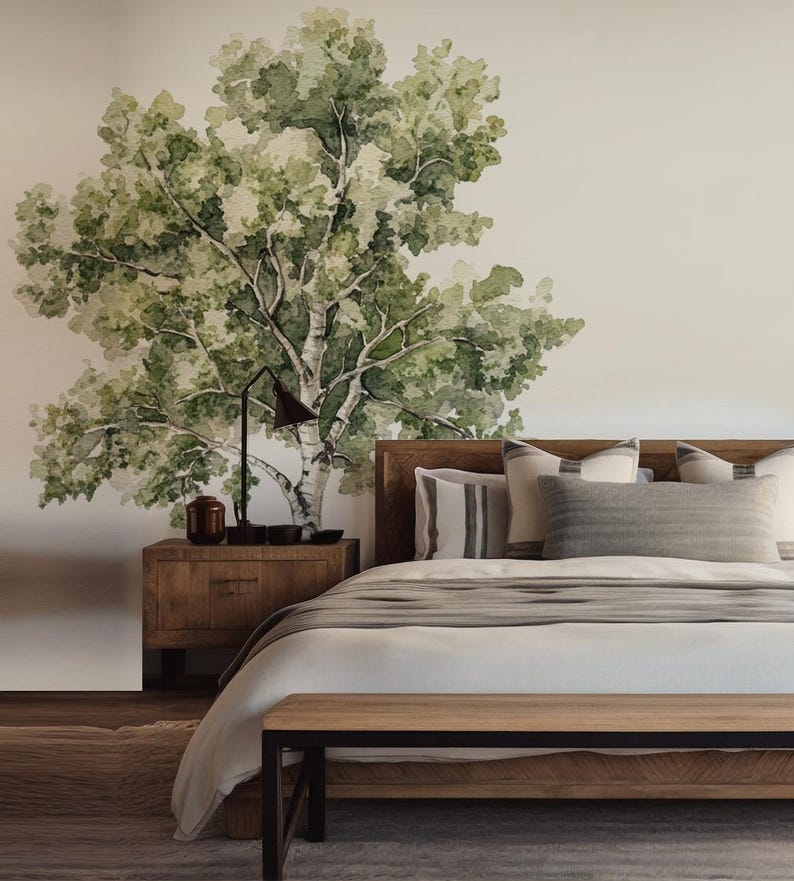 May include: A bedroom with a watercolor mural of a tree on the wall. The room features a wooden bed frame, nightstand, and bench. The bed is made with white linens and gray pillows. A black lamp and decorative items sit on the nightstand.