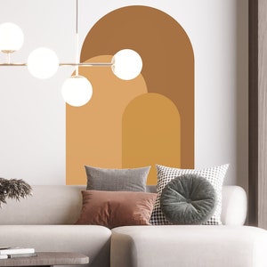 May include: A white sectional sofa with three pillows, one brown, one gray, and one black and white patterned pillow. The sofa is in front of a white wall with a large brown, orange, and yellow abstract arch design.