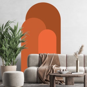 May include: A living room interior with a couch, a coffee table, a potted plant, and a wall decal featuring three overlapping arches in shades of orange and brown.