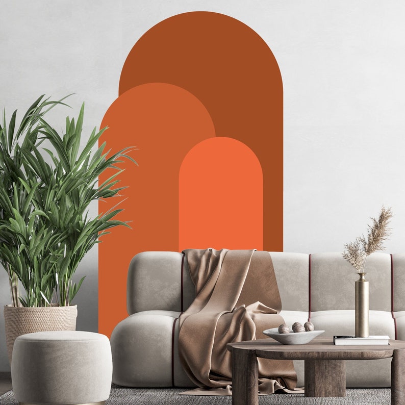 May include: A living room interior with a couch, a coffee table, a potted plant, and a wall decal featuring three overlapping arches in shades of orange and brown.