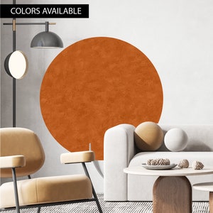 Puede incluir: Un gran adhesivo de pared redondo de color naranja-marrón con un acabado texturizado. El adhesivo está en una pared blanca detrás de un sofá blanco con cojines de color beige. El sofá está en un salón con una mesa de café y una silla.