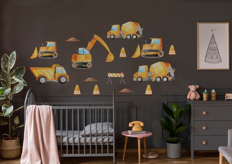 May include: A nursery room with a gray crib and a dresser with gold drawer pulls. The walls are decorated with yellow construction vehicle decals, including a cement mixer, a bulldozer, and an excavator. There are also orange traffic cones and a barricade.
