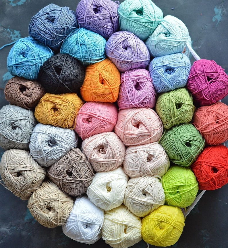 Puede incluir: Una colecci&oacute;n de ovillos de lana coloridos en varios tonos, incluyendo azul, morado, verde, naranja, rosa y amarillo. La lana est&aacute; cuidadosamente dispuesta, sugiriendo un proyecto de artesan&iacute;a o tejido. La imagen muestra una variedad de colores y texturas.