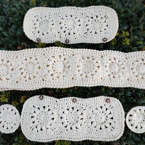 Puede incluir: Juego de ganchillo color crema con dise&ntilde;o floral. El conjunto incluye una pieza rectangular larga, dos piezas rectangulares m&aacute;s peque&ntilde;as con botones y dos piezas circulares. Las piezas est&aacute;n dispuestas sobre follaje verde.