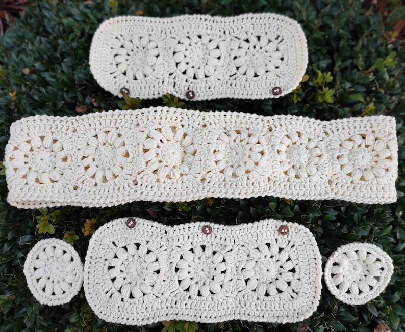 Puede incluir: Juego de ganchillo color crema con dise&ntilde;o floral. El conjunto incluye una pieza rectangular larga, dos piezas rectangulares m&aacute;s peque&ntilde;as con botones y dos piezas circulares. Las piezas est&aacute;n dispuestas sobre follaje verde.