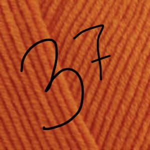 May include: A close-up view of vibrant orange yarn featuring a distinct ribbed or knitted texture. The number 37 is written in black ink directly over the center of the orange fabric, serving as a clear identifier for this specific yarn color.