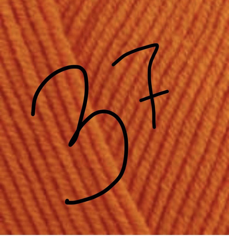 May include: A close-up view of vibrant orange yarn featuring a distinct ribbed or knitted texture. The number 37 is written in black ink directly over the center of the orange fabric, serving as a clear identifier for this specific yarn color.