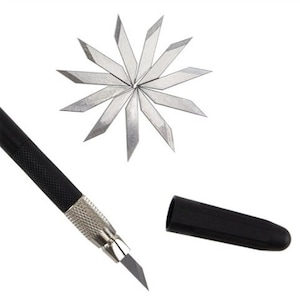 May include: A black craft knife with a silver blade and a black protective cap. The knife is shown with a pack of 12 replacement blades.