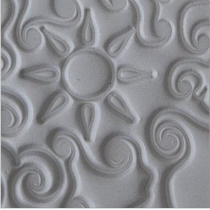 May include: A white ceramic tile with a raised design of a sun with rays and swirling patterns.