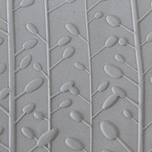 May include: A close-up of a white ceramic tile with a raised embossed pattern of stylized branches and leaves.