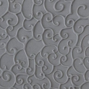 Puede incluir: Una estera de hornear de silicona gris con un patrón repetitivo de remolinos y rizos. La estera está diseñada para usarse con fondant, pasta de goma y otras decoraciones comestibles.