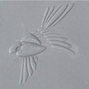 May include: A gray ceramic tile with a raised design of a stylized fish. The fish has a detailed body and fins.
