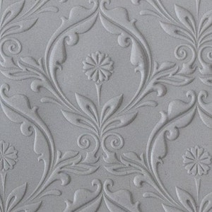 Puede incluir: Un papel tapiz blanco en relieve con un patrón repetitivo de diseños florales estilizados. El patrón presenta una flor central de cuatro pétalos y hojas que se curvan y retuercen.