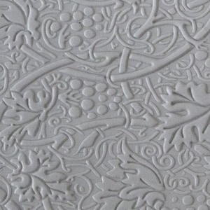 May include: A close-up of a gray, textured surface with a repeating pattern of grapes, leaves, and vines. The design is embossed, creating a three-dimensional effect. The overall aesthetic is reminiscent of classical or vintage design.