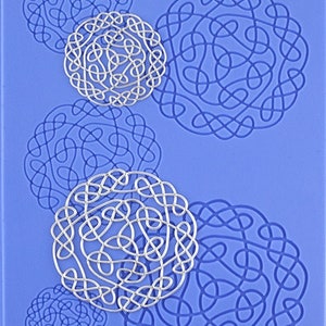 Puede incluir: Una estera de horneado de silicona azul con cinco diseños decorativos circulares, plateados e intrincados. Los diseños están hechos de líneas entrelazadas que se asemejan a nudos.