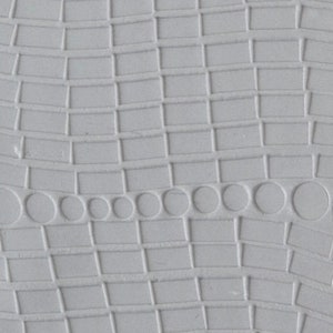 Puede incluir: Primer plano de una superficie gris texturizada con una fila de pequeños círculos en relieve en una línea curva.