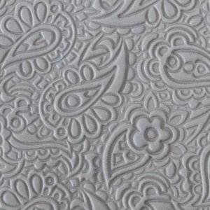 Op de afbeelding: Een close-up van een grijze, geëmbosseerde stof met een paisley-patroon. De stof heeft een textuur en een herhalend patroon van paisley-vormen.